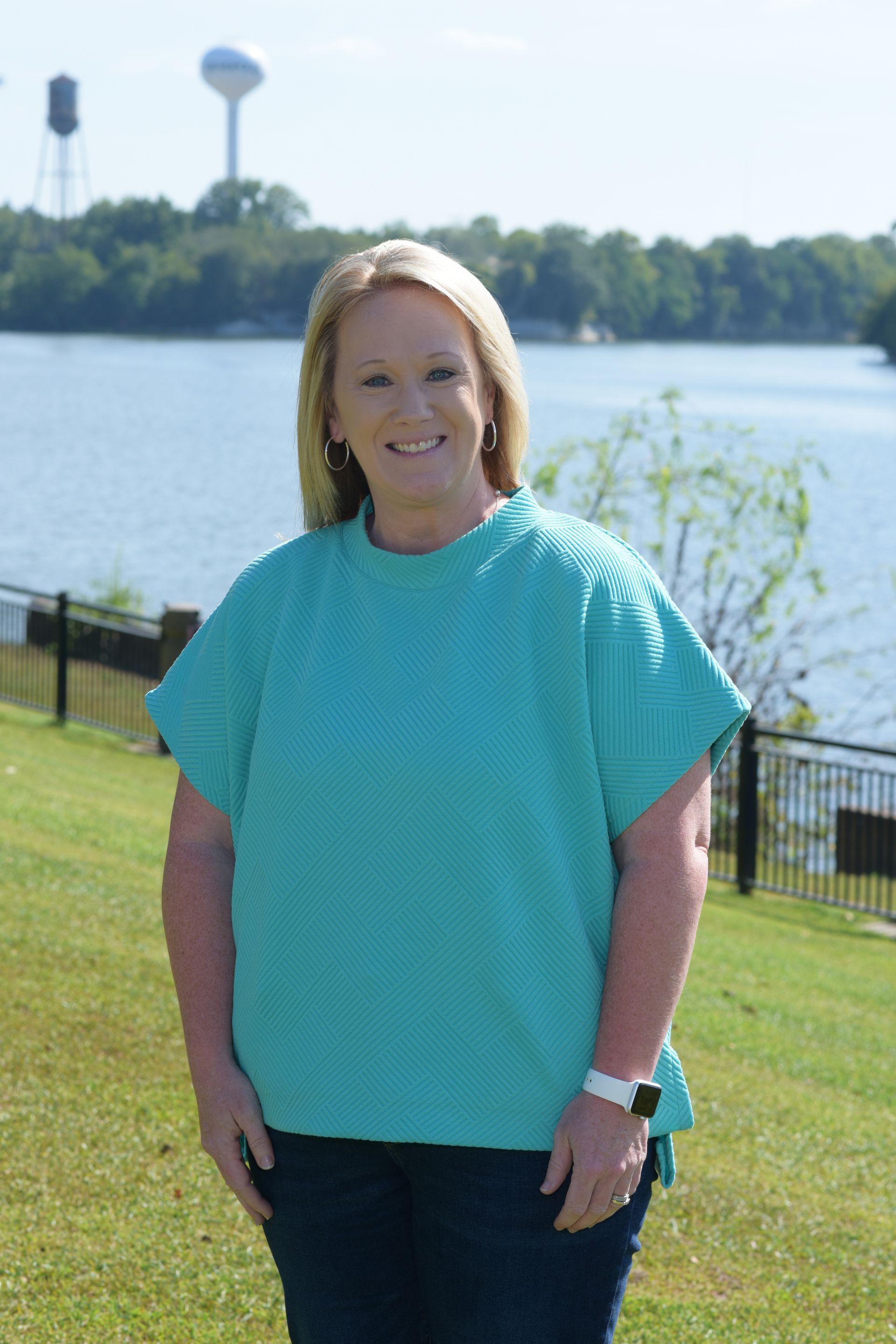 A woman with blonde hair is wearing a gray sweater and smiling.