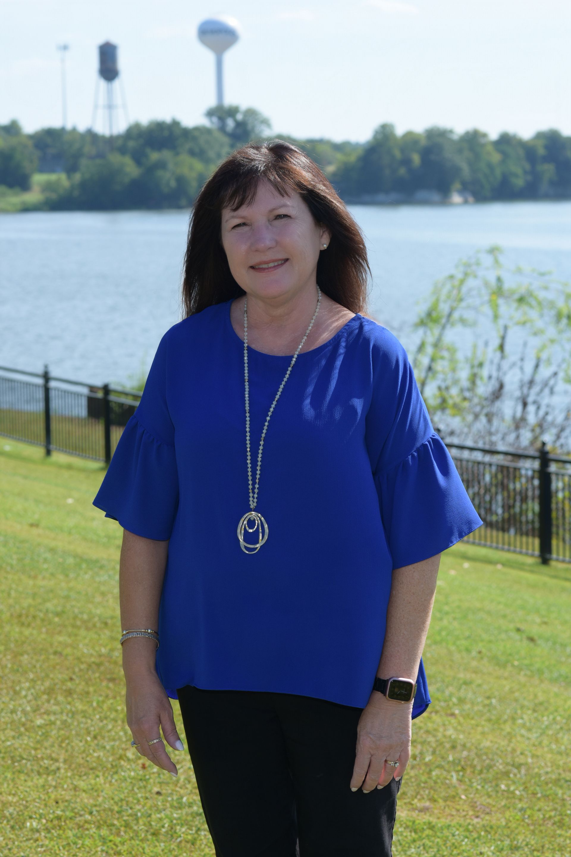 A woman with long brown hair is wearing a black vest and a necklace.