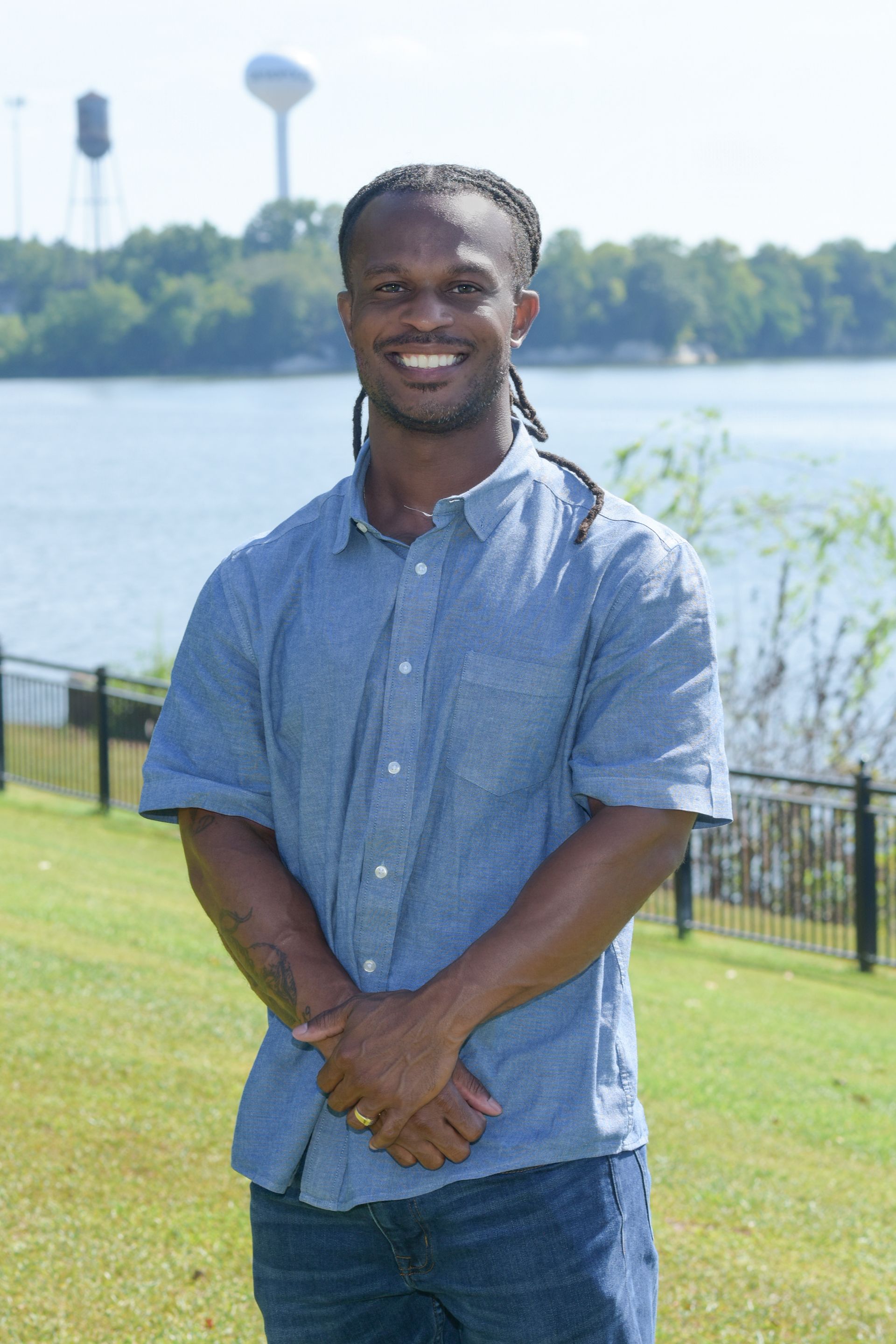 A man with dreadlocks is wearing a white shirt and smiling for the camera.
