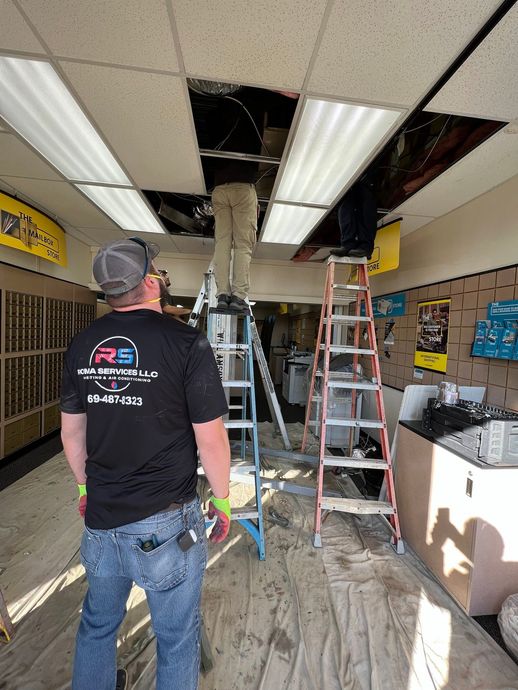 Three technicians work on electrical wiring in the ceiling tiles of a room, using two stepladders.