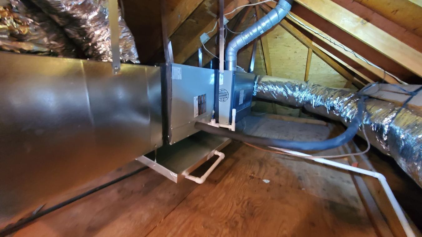 An attic view of an HVAC air handler unit connected to silver metal and insulated flexible ductwork.