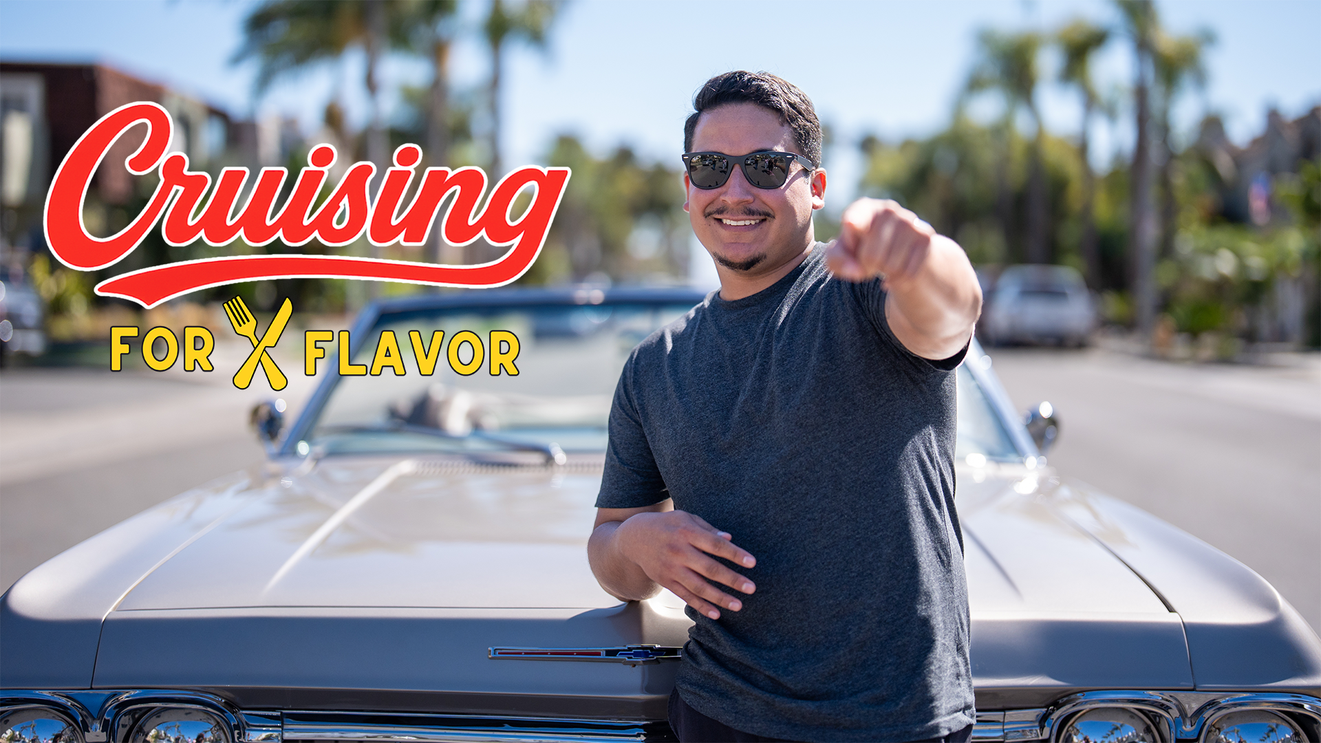 Manny Cabrera, host of Cruising for Flavor, in front of a classic car, pointing and smiling on a sun
