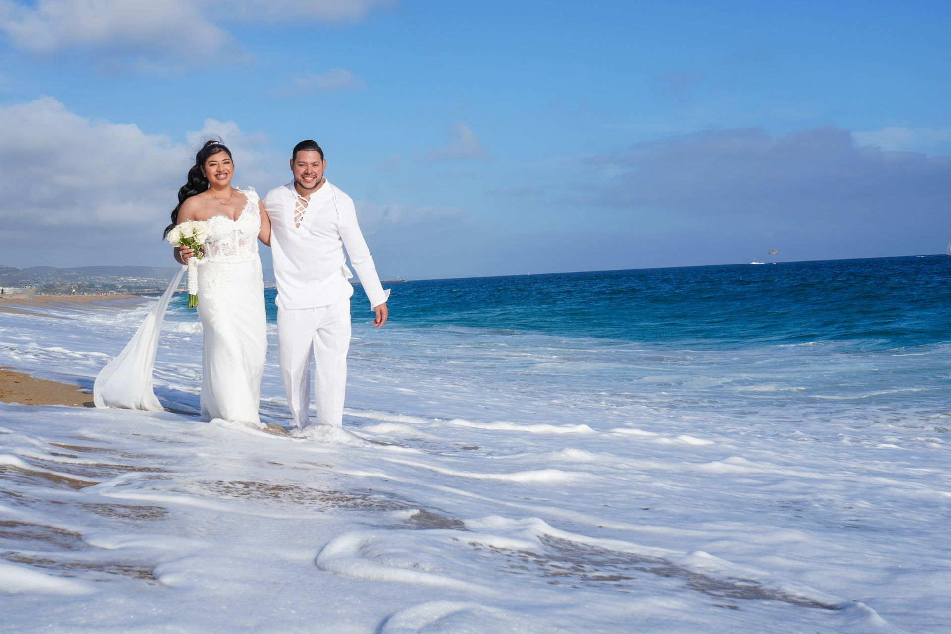 Bride and groom walking hand in hand on whitewash shoreline at boho beach wedding in Newport, CA