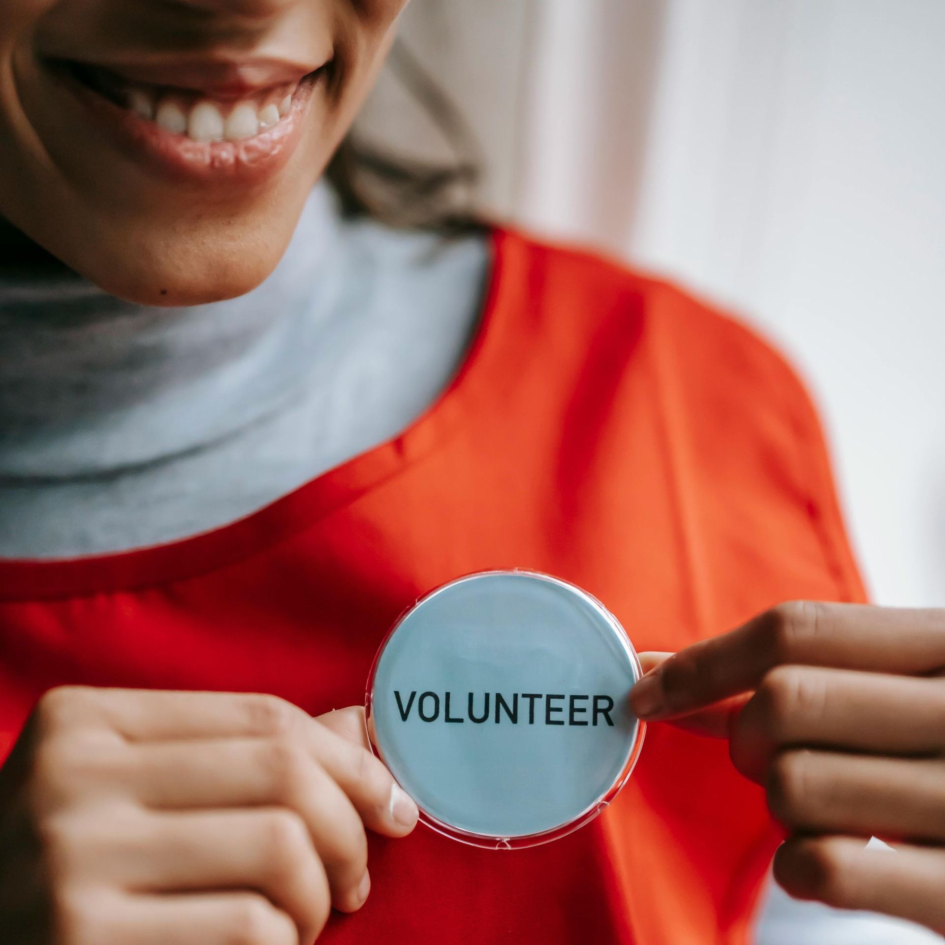 A woman in a red shirt is holding a volunteer badge.