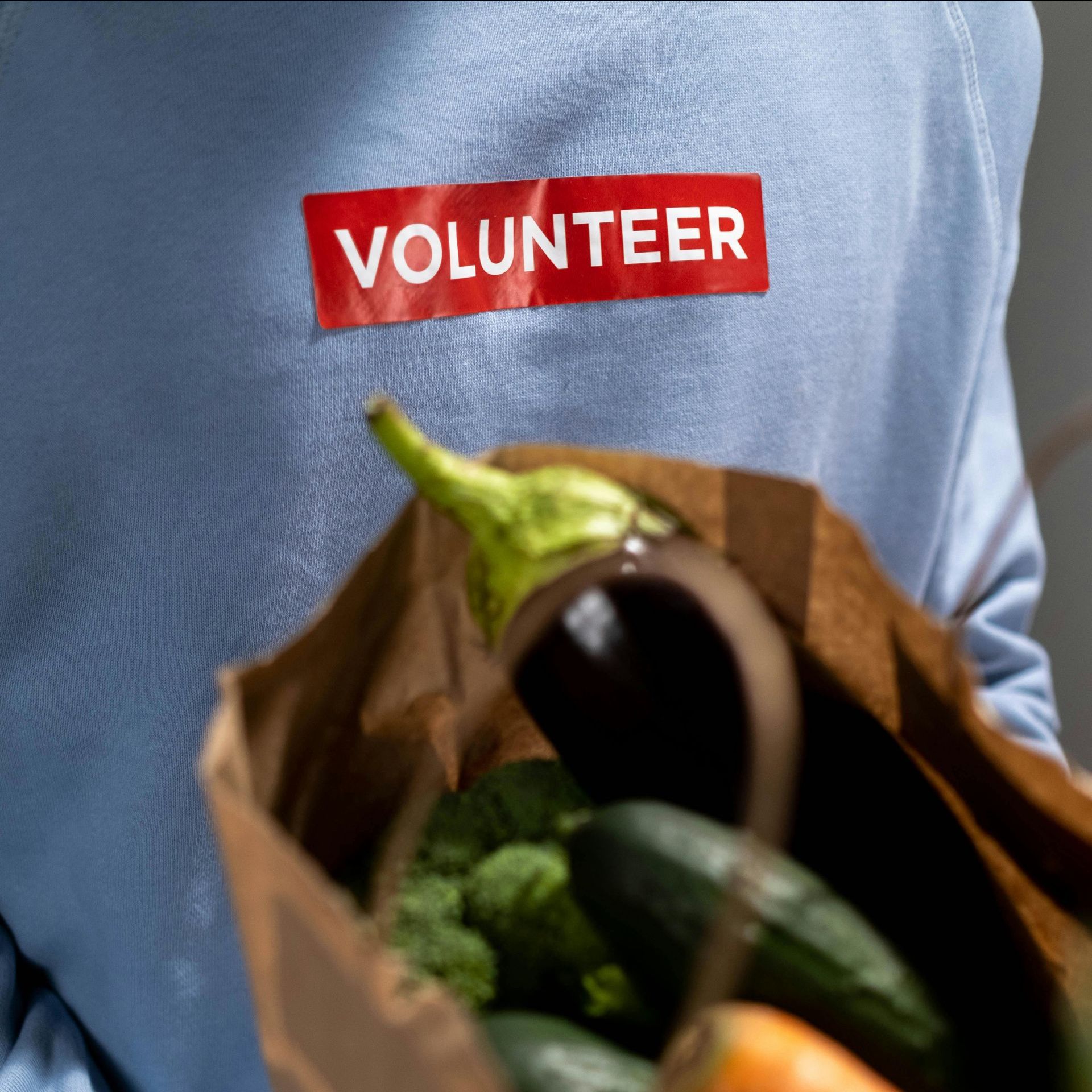 A person wearing a volunteer shirt is holding a bag of vegetables.