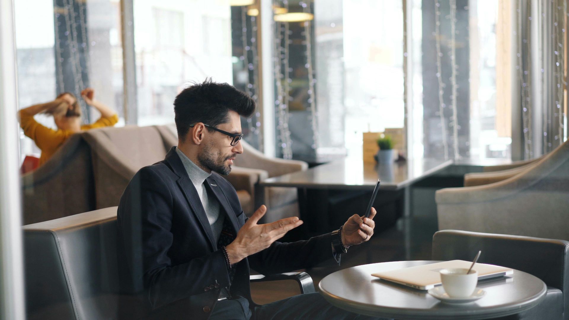 A man in a suit is sitting at a table using a tablet computer working with a client.