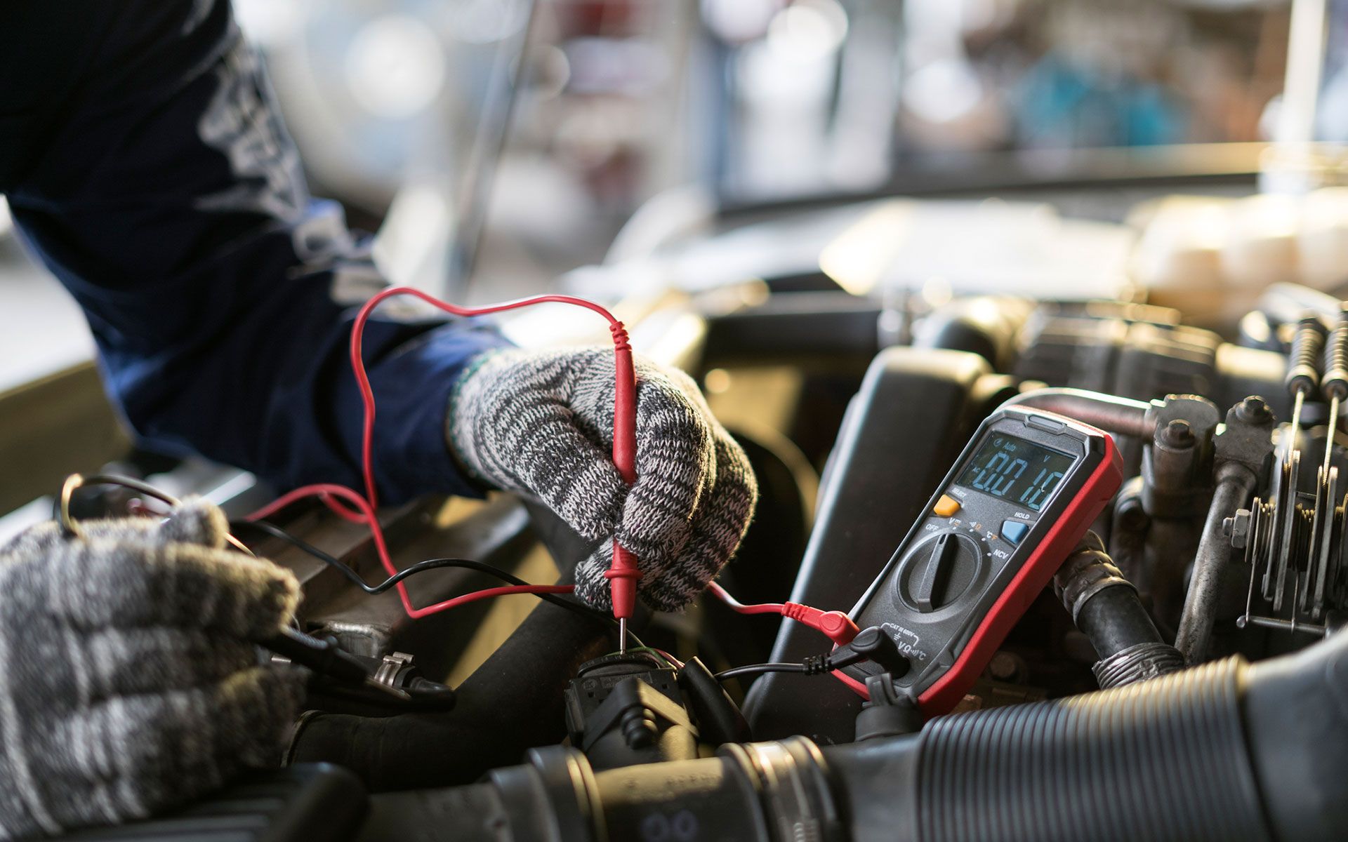 A mechanic is working on a car engine with a multimeter.