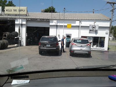 Two cars are parked in front of a wells tire supply store.