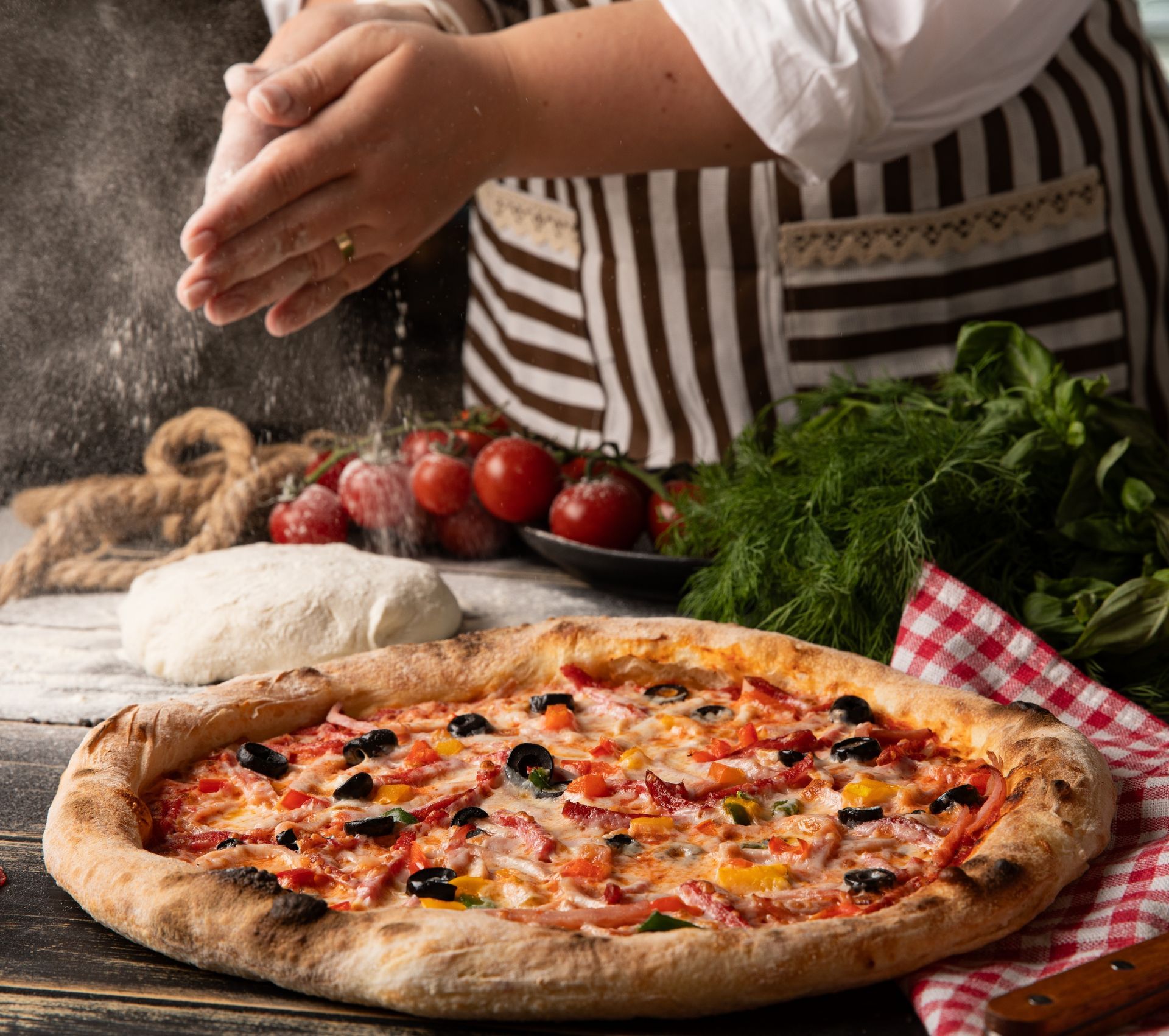 Chef dusting flour on hands above a pizza