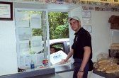 Man in uniform hands a food order to a person in a car at a drive-through window.