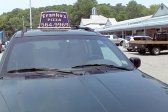 Car with a rooftop sign for Frank's Pizza parked in front of a shopping area.