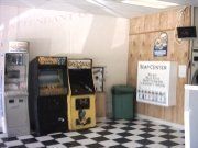 Laundromat corner with arcade games, a trash can, and a sign on a wood-paneled wall, checkerboard floor.