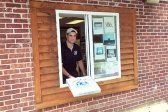 Man handing out a bag from a drive-thru window framed by wood, brick building.