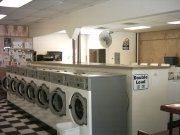 Row of washing machines in a laundromat; white and gray, tiled floor.
