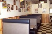 Restaurant booth seating with gray upholstered walls and black/white checkered floor. Posters and pictures on the wall.