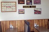 A diner interior with wood paneling, booths, tables, and car-themed artwork on the wall.