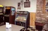 A diner interior with a jukebox, arcade games, a checkered floor, and wood paneling.