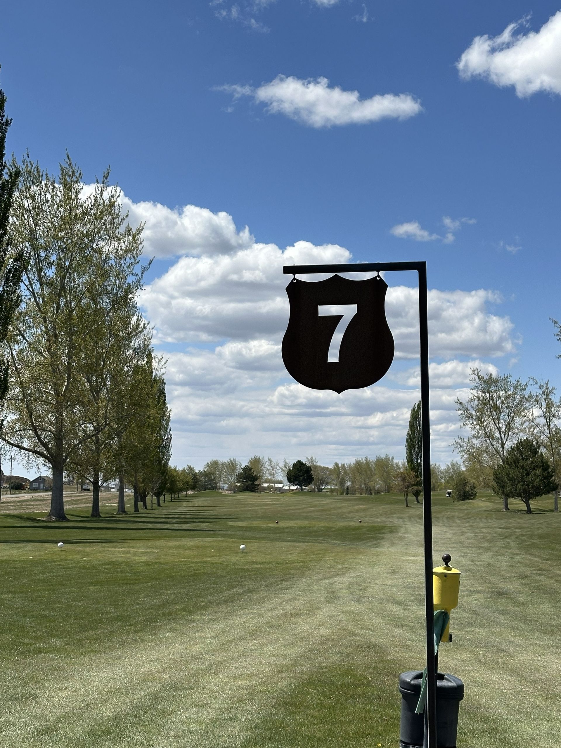 Golf course sign with number 7 beside a grassy fairway under a blue sky