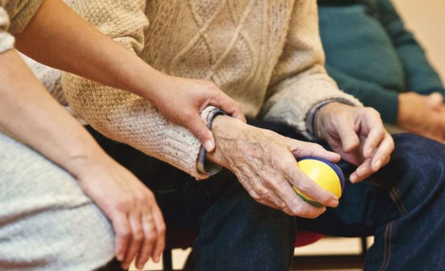 picture of caregiver's hand assisting elderly holding small ball