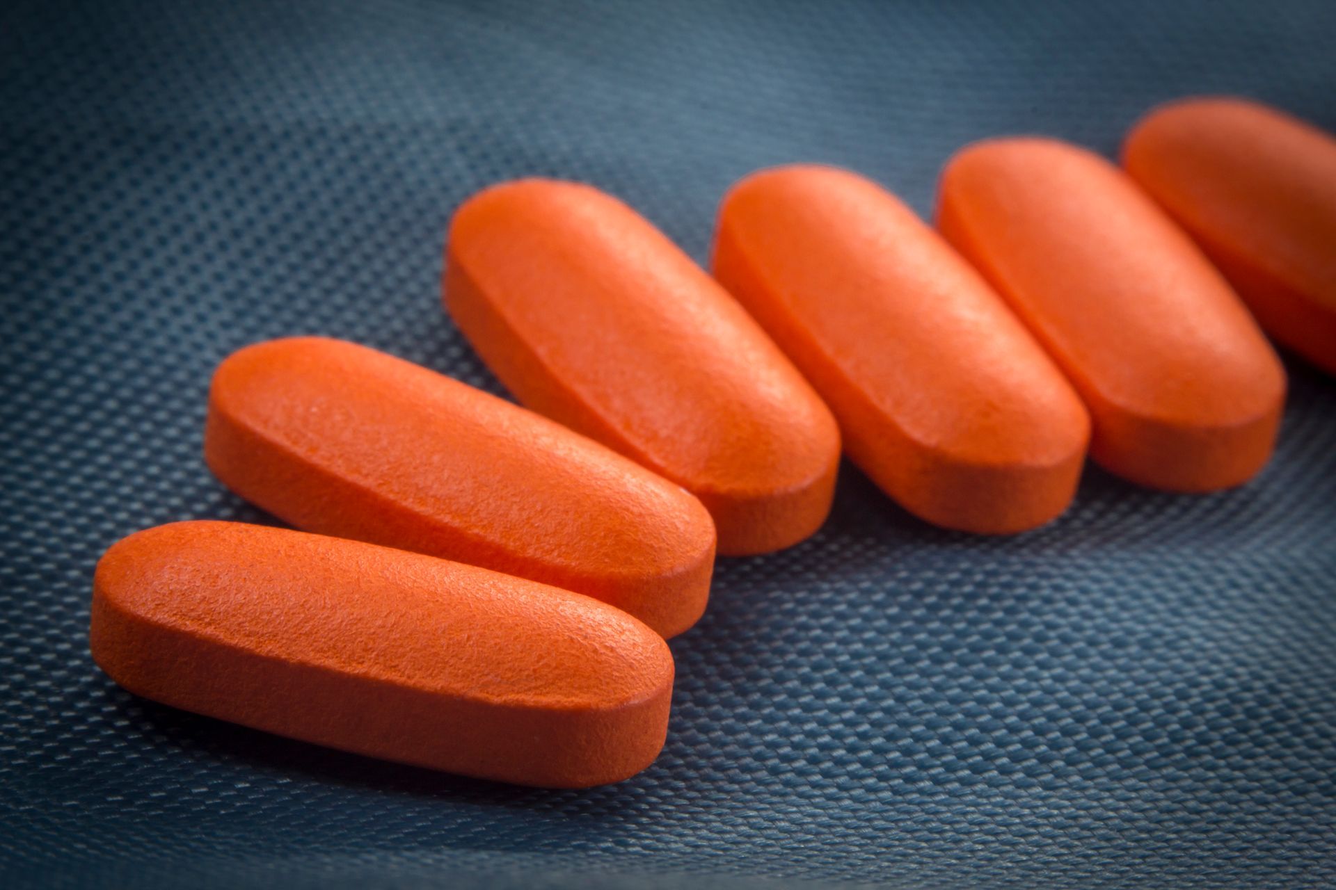 A row of orange pills on a blue surface.