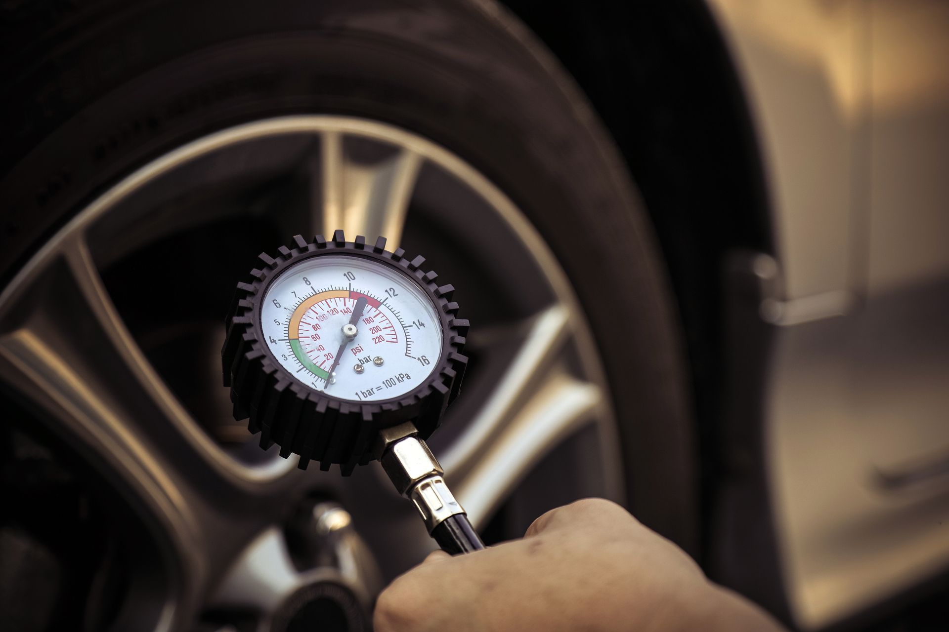 Person checking tire pressure with a gauge near a car's wheel. | Rocky Mountain Car Care