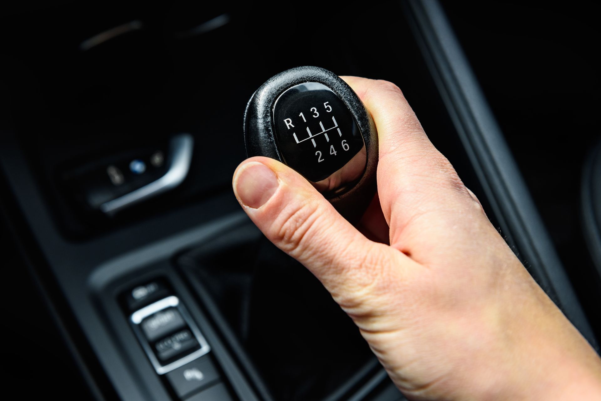 Hand holding a black gear shift knob in a car; numbered gear positions are visible. | Rocky Mountain Car Care
