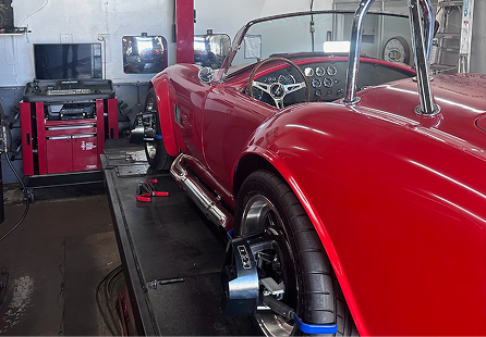 Red sports car on a lift, undergoing wheel alignment in a garage. | Rocky Mountain Car Care