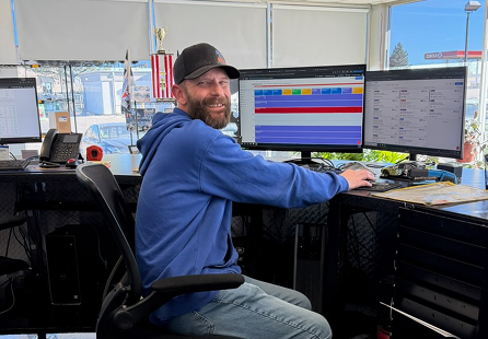 Man in blue hoodie at a desk with two computer monitors, looking toward the camera. | Rocky Mountain Car Care