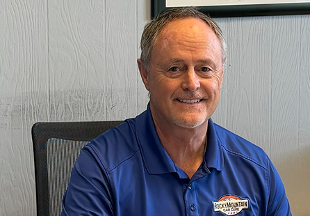 Man wearing blue polo shirt smiles at the camera in an office setting. 