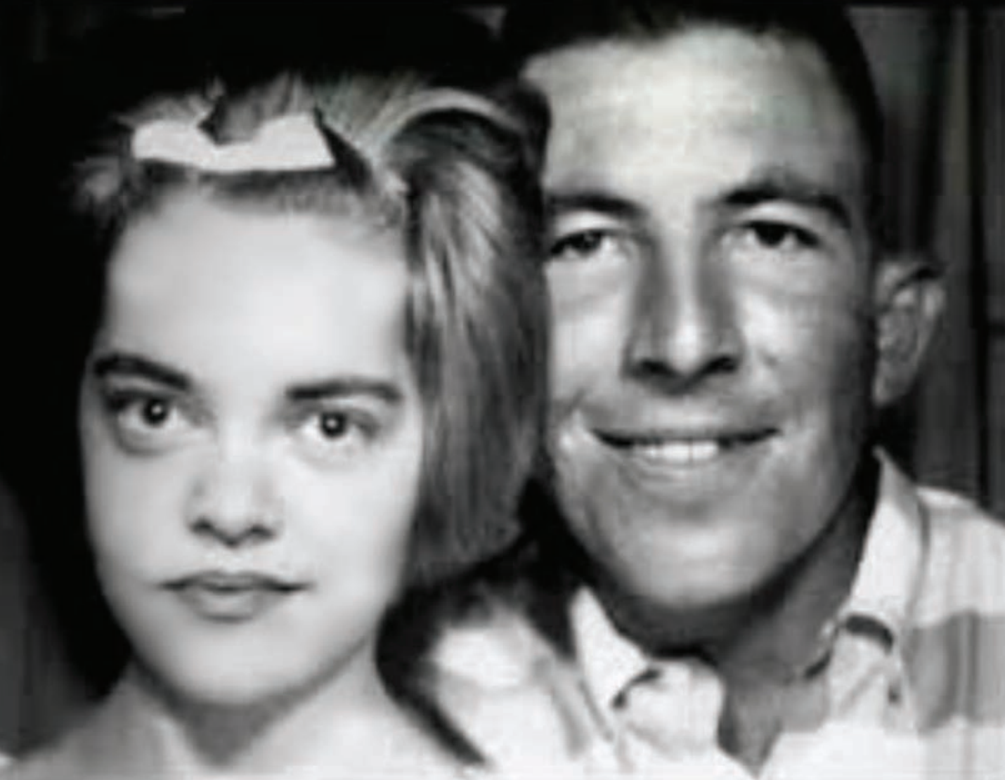 Black and white photo of a young woman with a bow in her hair next to a smiling man.