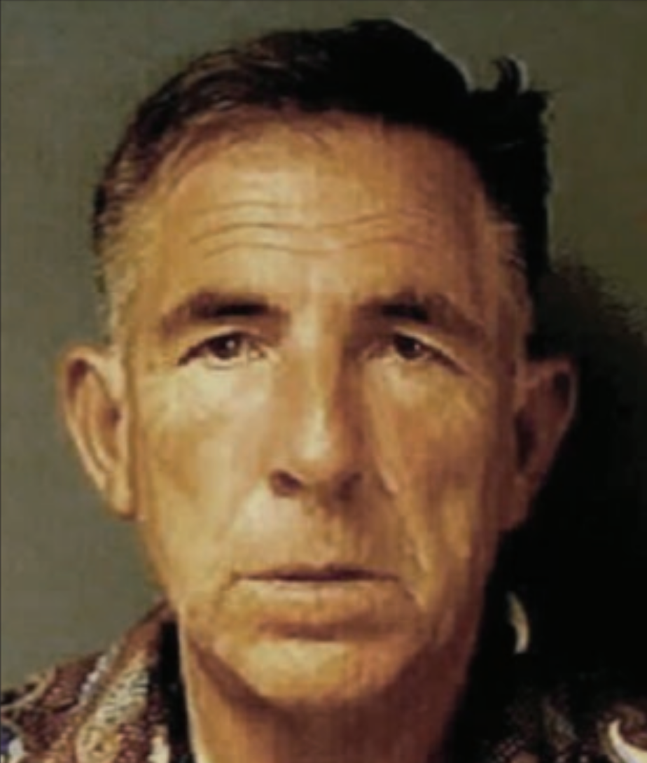 Portrait of a light-skinned man with short brown hair. He has a serious expression and is wearing a patterned shirt.