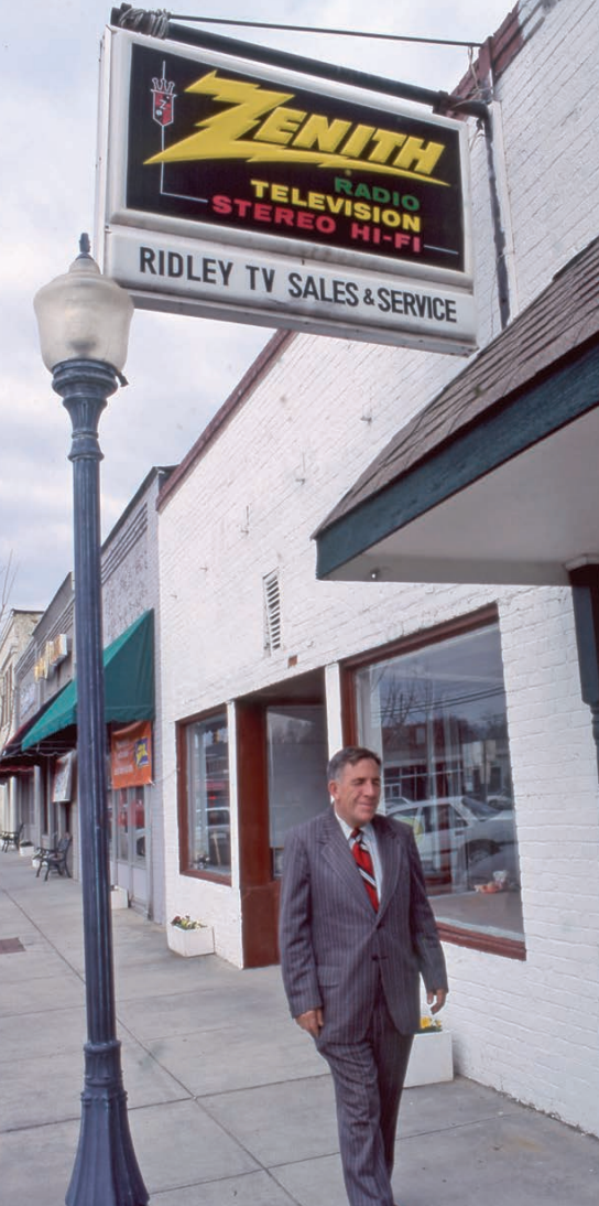 Man in a suit walks past a Zenith TV sales and service store. The sign reads