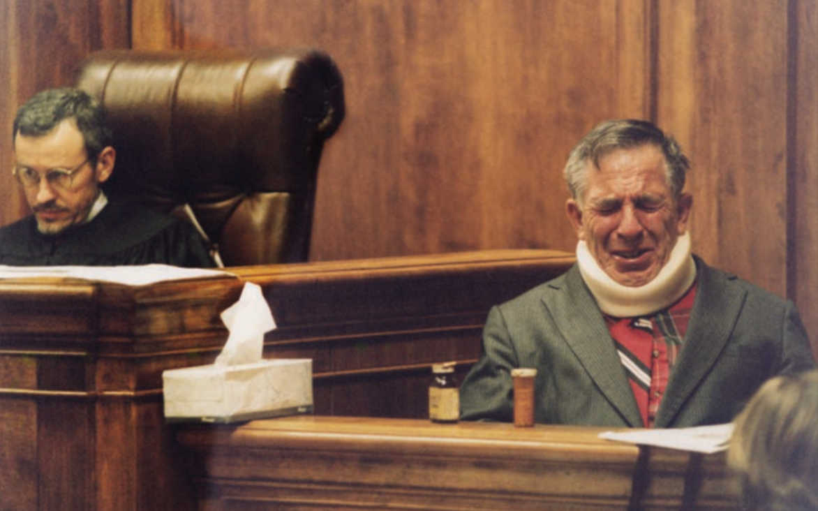 Man with neck brace crying in a courtroom, judge in the background.