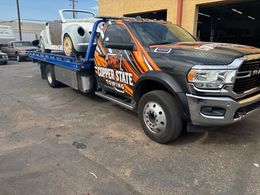 Tow truck with a partially restored convertible. The truck is parked outside a building.
