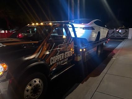 White Tesla on a Copper State Towing flatbed truck at night.