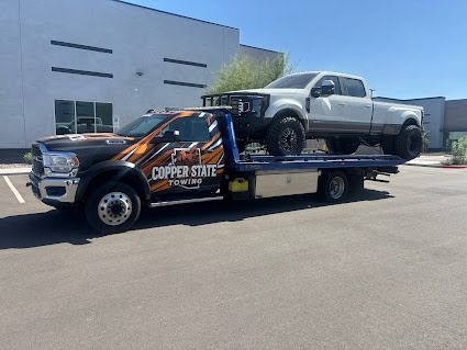 Tow truck with a white pickup truck on its flatbed, parked in a lot.