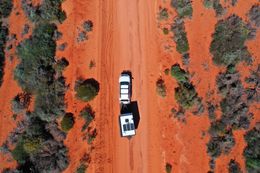 White truck towing a trailer on a red dirt road through arid, green brush.