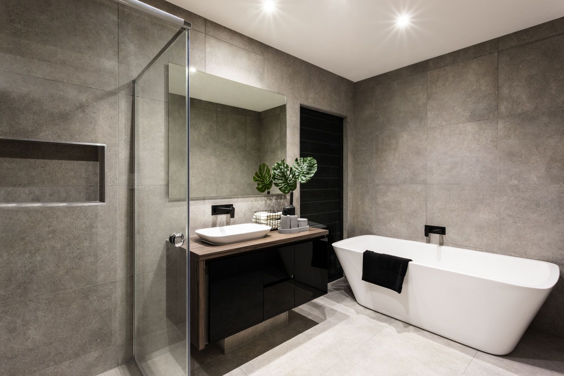 Modern bathroom with gray tile walls, glass shower, black vanity, and a white freestanding tub.