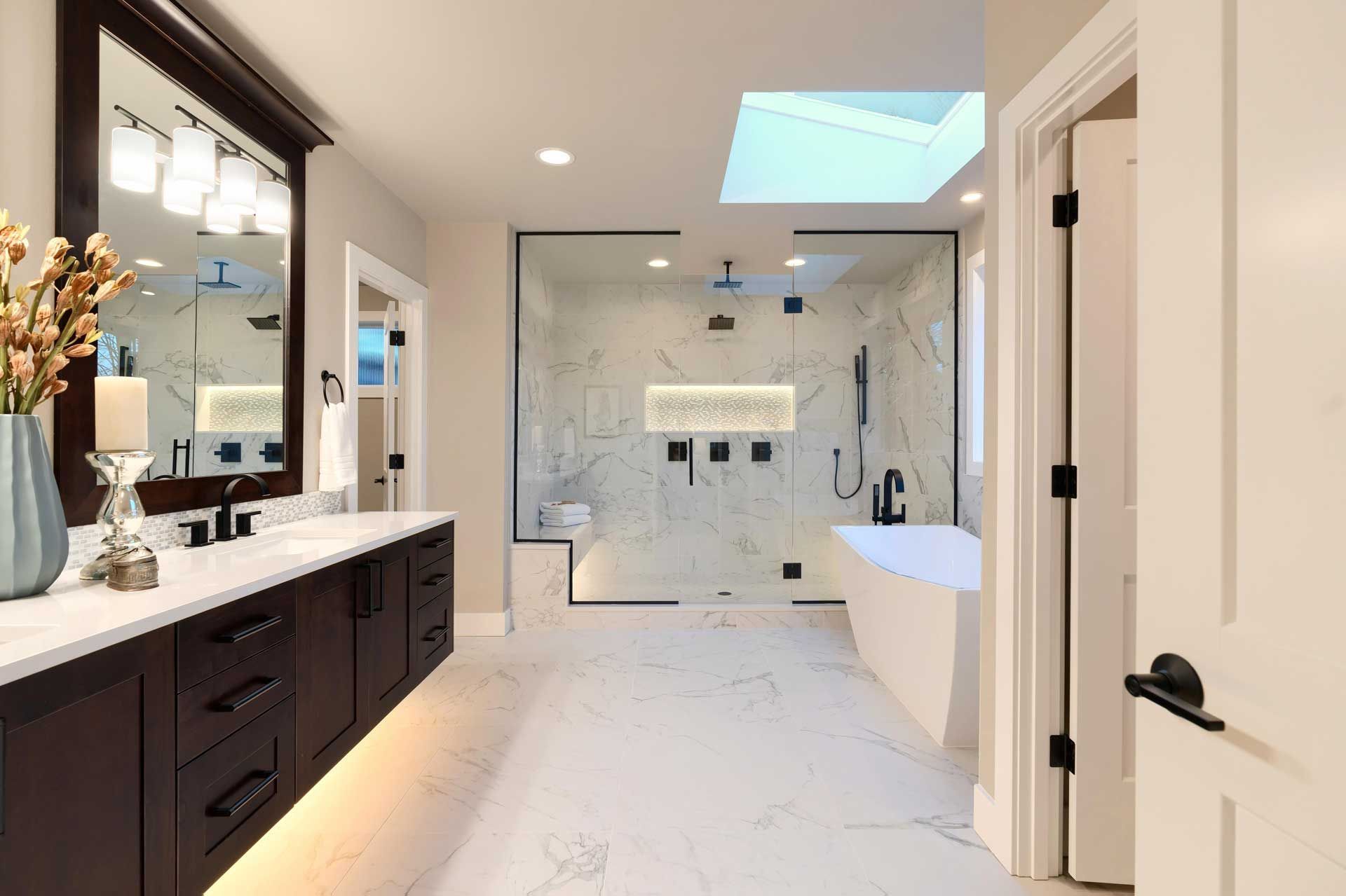 A finished custom bathroom renovation featuring brown cabinets, marble, a shower, and a tub.
