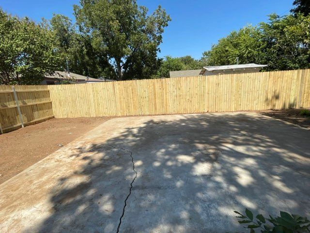 A wooden fence surrounds a concrete driveway in a backyard.