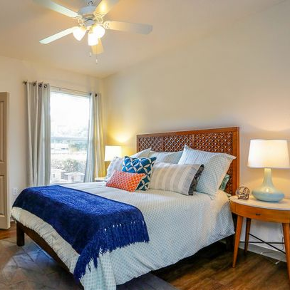 Bedroom with bed, dresser, lamps, window, and closet. Warm tones with blue accents.