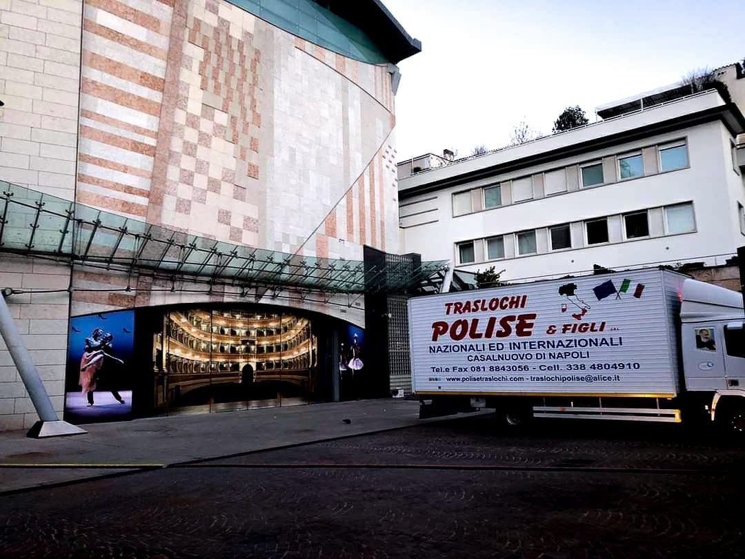 Tenda e furgone della polizia davanti a un edificio, con uno striscione con la scritta 