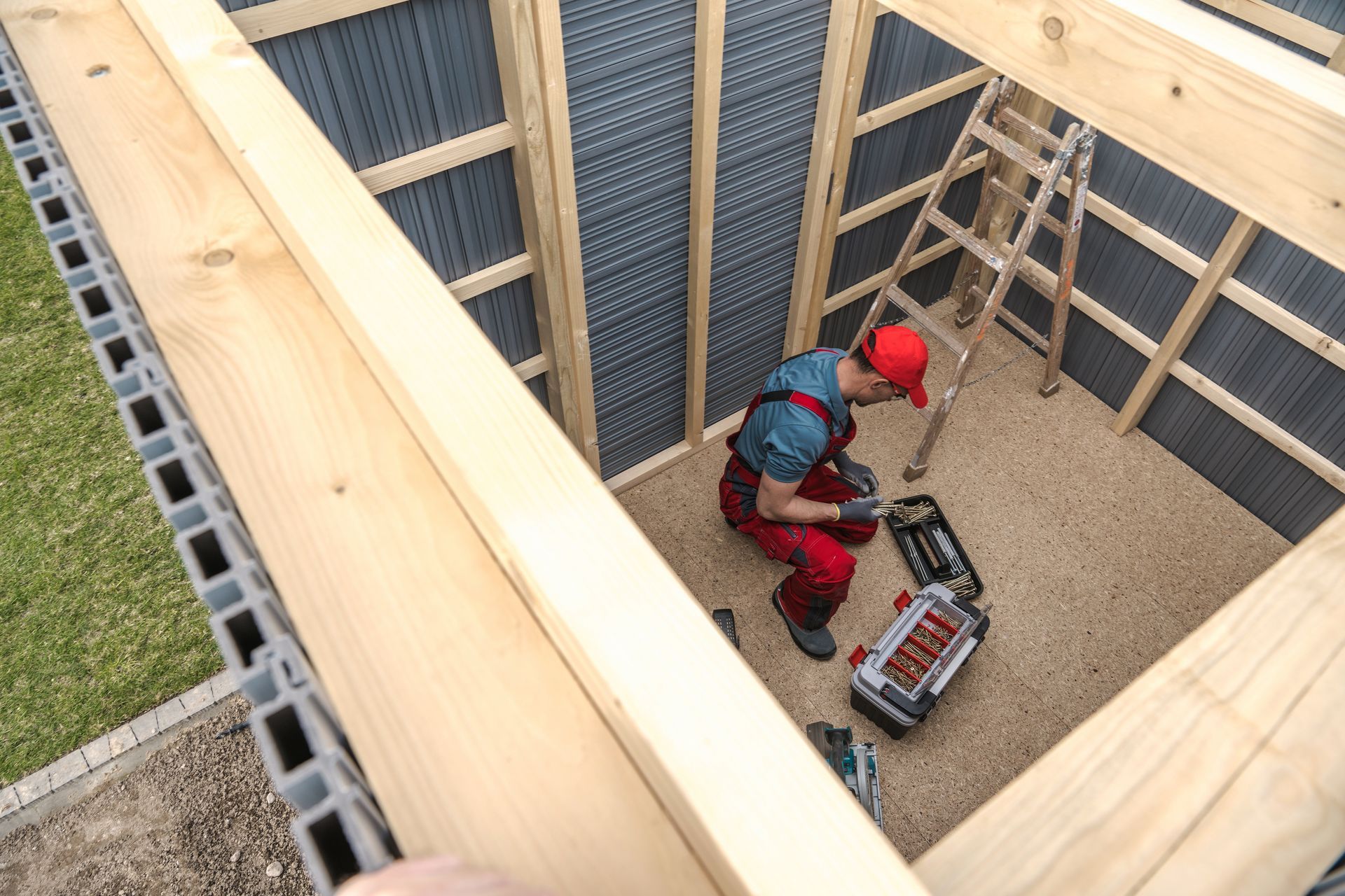 A handyman assembling a wooden shed in a backyard.