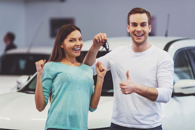 Due persone sorridenti che tengono in mano le chiavi di un'auto nello showroom di una concessionaria.