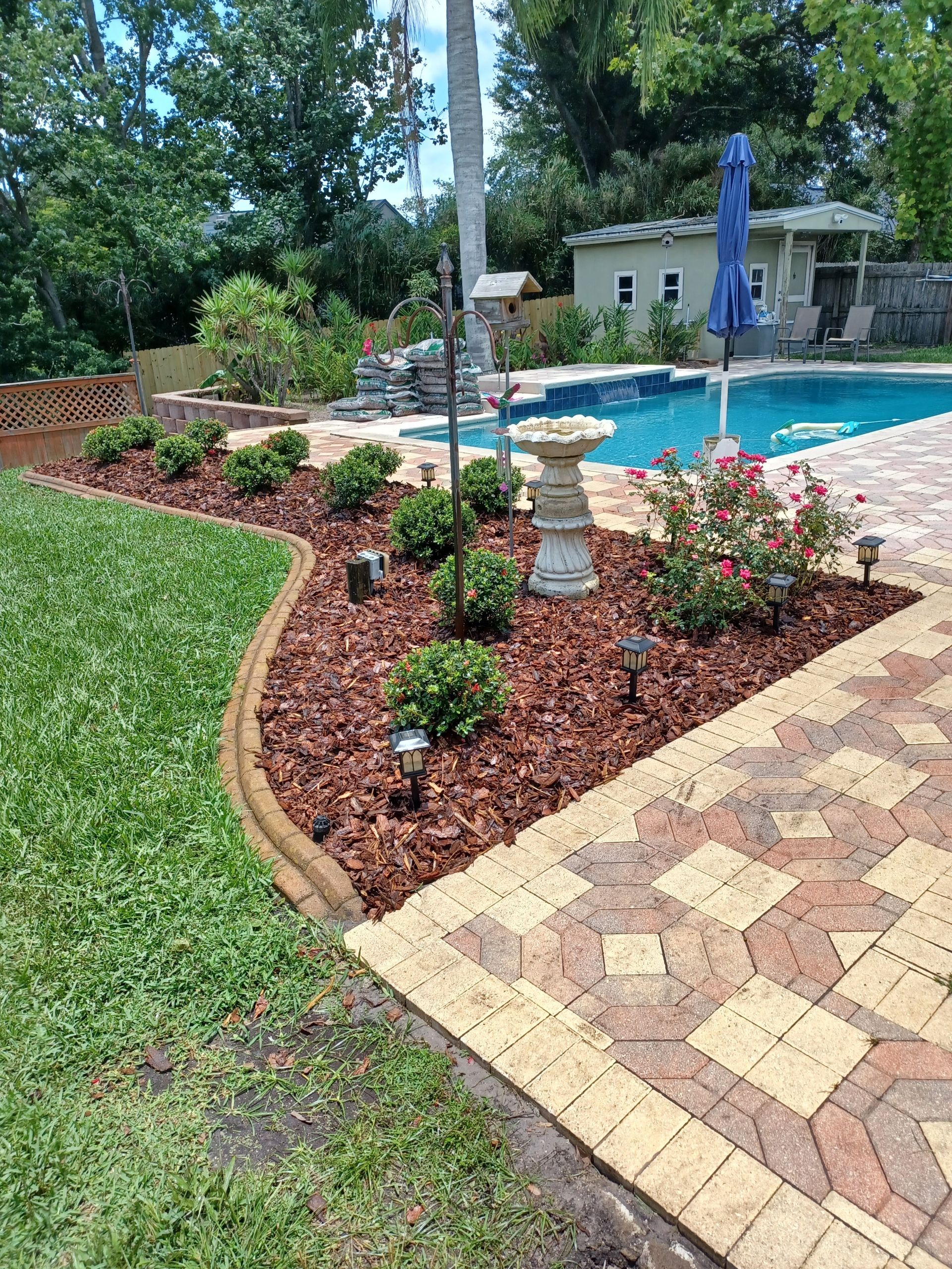 A brick walkway leading to a swimming pool in a backyard.