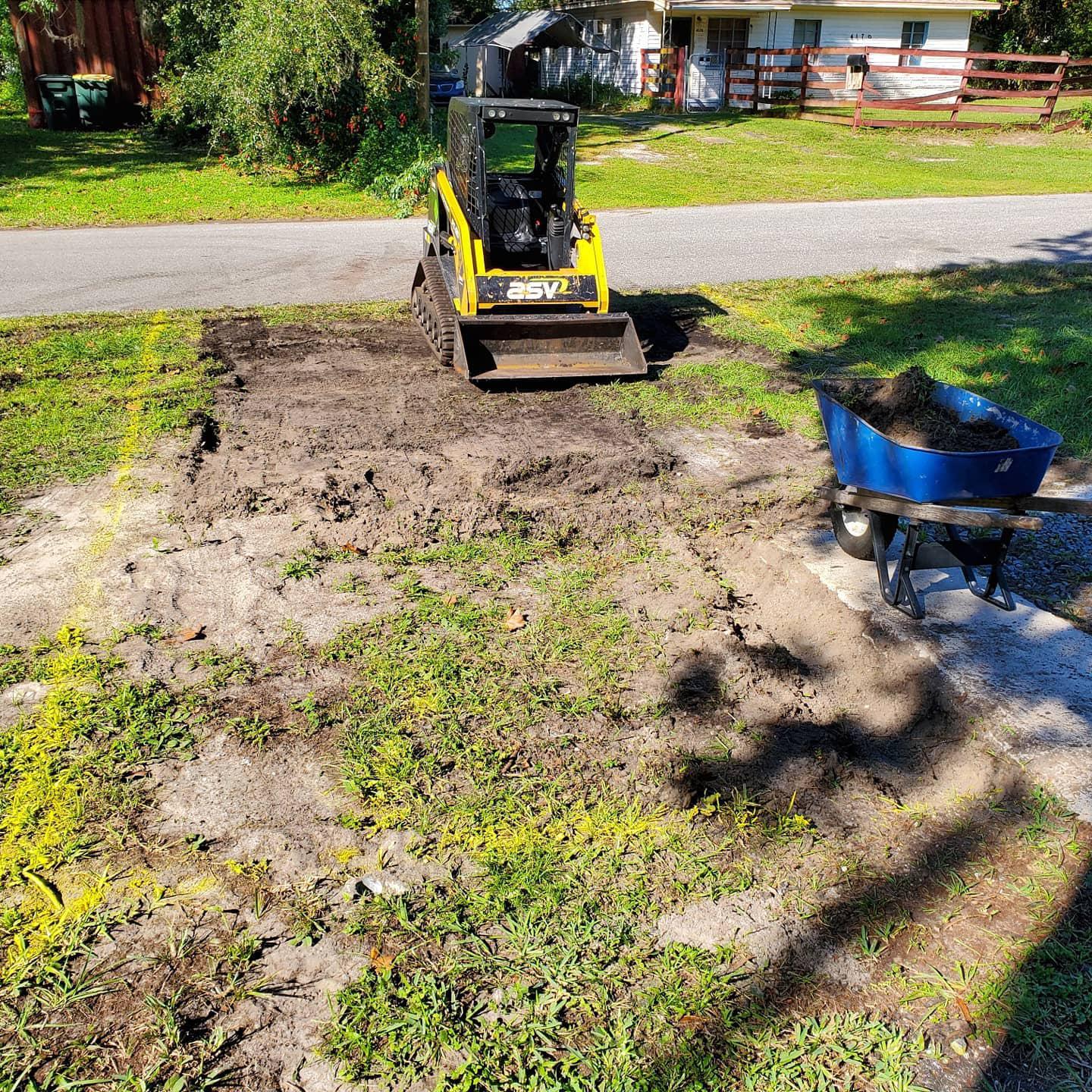 A bulldozer is moving dirt in a yard next to a wheelbarrow.