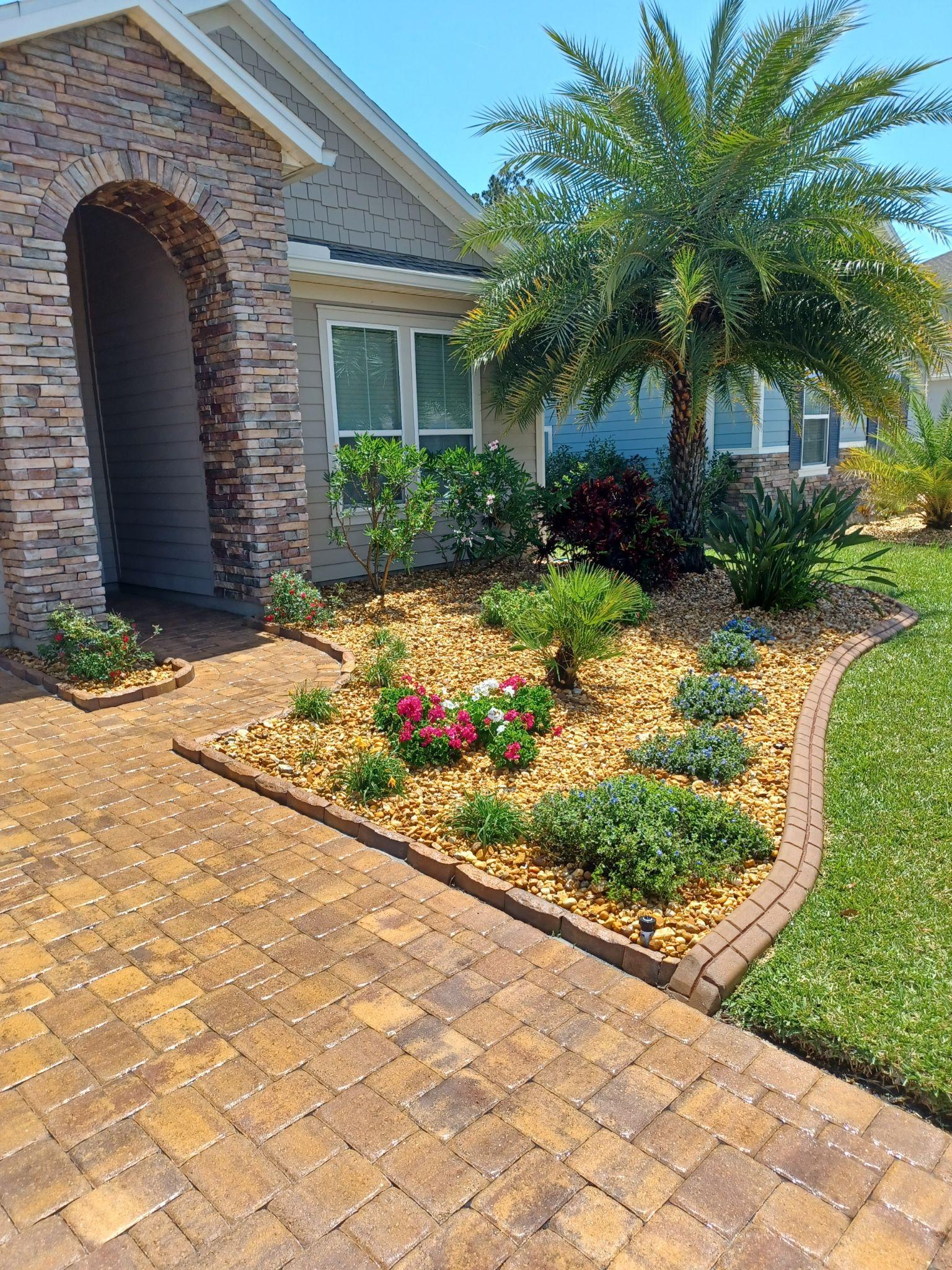 A brick driveway leading to a house with a garden in front of it.