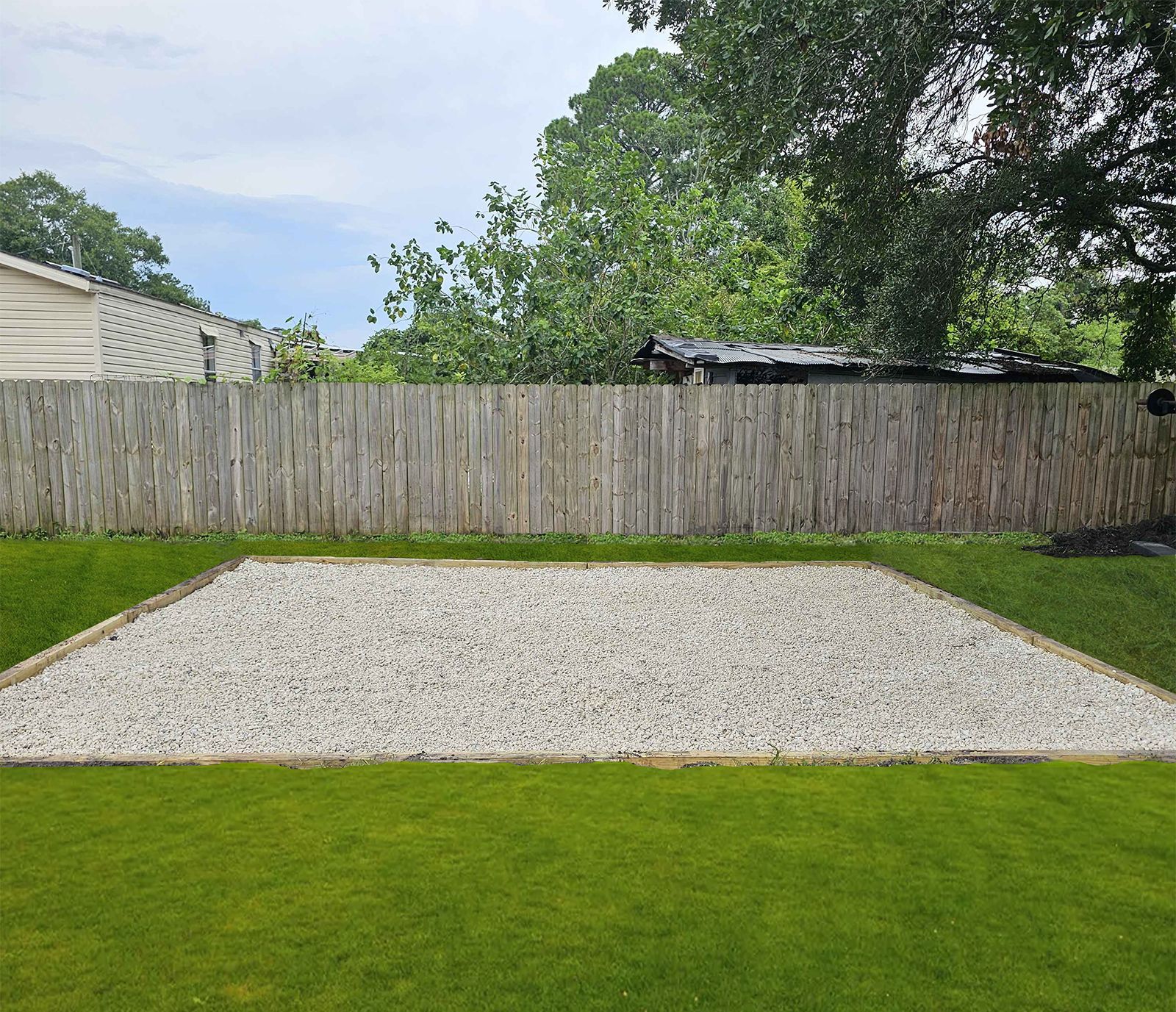 A gravel area in a backyard with a wooden fence in the background