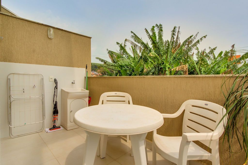 Conjunto de móveis brancos para área externa em uma varanda, com um bebedouro e vegetação exuberante ao fundo.