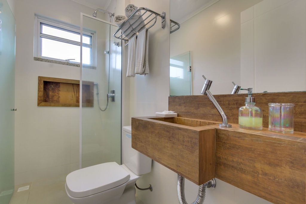 Banheiro moderno com pia de madeira, box de vidro e vaso sanitário branco.